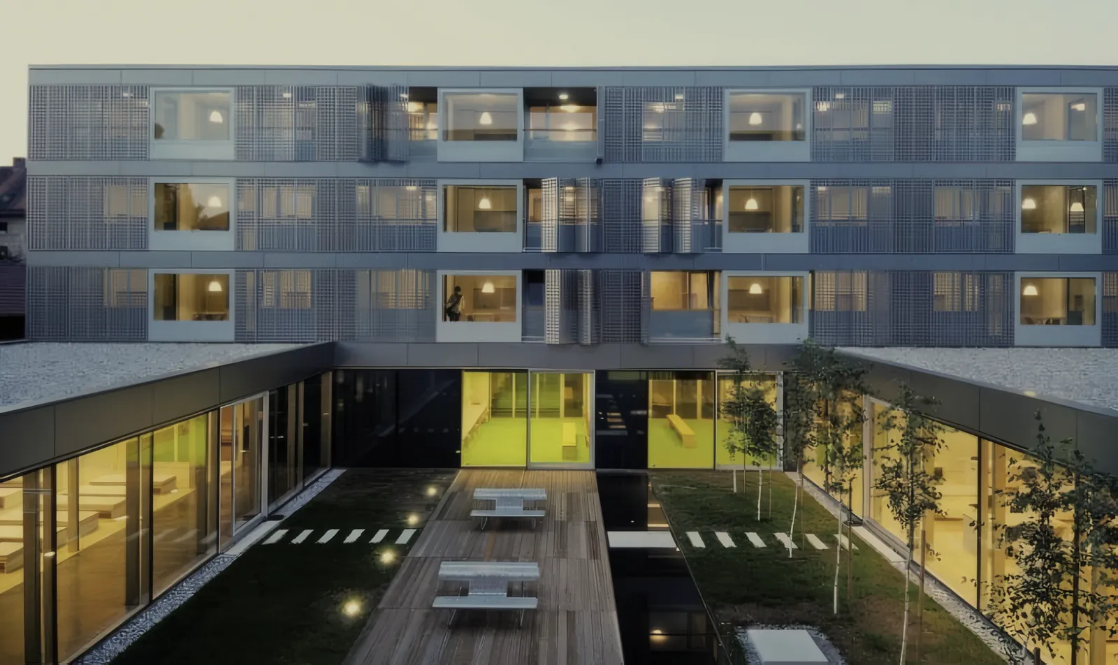 Reference photograph of a student residence courtyard with timber decking, benches and glazed common rooms at dusk